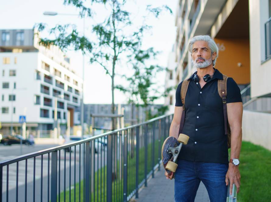 älterer Mann mit skateboard in urbanem setting